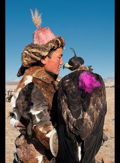 a man holding a large bird in his hand and wearing a hat with feathers on it