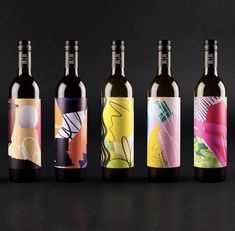 four bottles of wine are lined up on a black surface, one is empty and the other has an abstract design