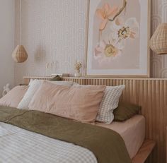 a bed with pink and green pillows in a bedroom next to a painting on the wall