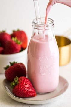 strawberry milk being poured into a glass jar with strawberries in the background on a plate