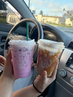 two people holding up starbucks drinks in their hand while sitting in the driver's seat of a car