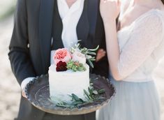 a newly married couple standing next to each other in front of a cake on a plate