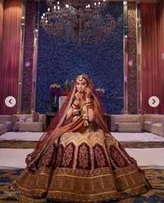 a woman in a red and gold bridal gown sitting on the floor with chandelier