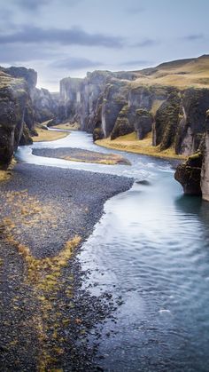 a river flowing through a lush green valley next to tall rocky cliffs and grass covered hillsides