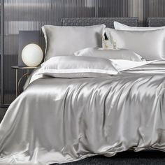 a bed with silver sheets and pillows on top of it in a bedroom next to a night stand