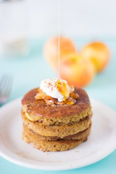 a stack of pancakes on a plate with whipped cream and peaches in the background