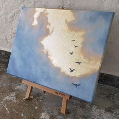 a painting on an easel with birds flying in the sky and clouds painted on it