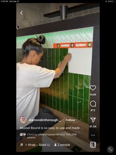 a woman writing on a white board in front of a green tiled wall