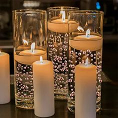 some candles are sitting in glass vases on a table with water and beads around them