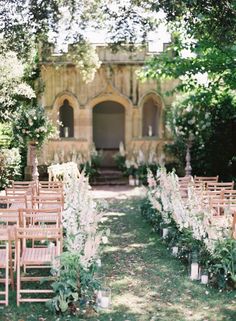 an outdoor ceremony setup with wooden chairs and flowers on the aisle, surrounded by greenery