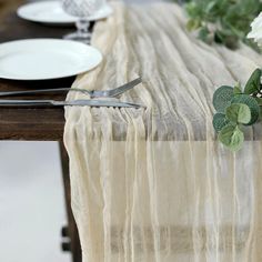 the table is set with silverware and white flowers on it, along with plates and utensils