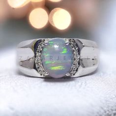 an opal and diamond ring sits on a white cloth with lights in the background