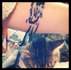 a cat laying on top of a table next to a person's arm with writing on it