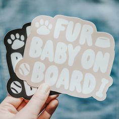 someone holding up two stickers with the words fur baby on board and paw prints