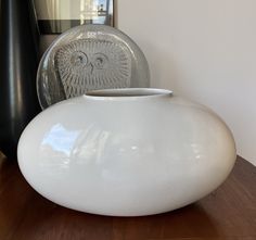 a white vase sitting on top of a wooden table next to a black vase with an owl face