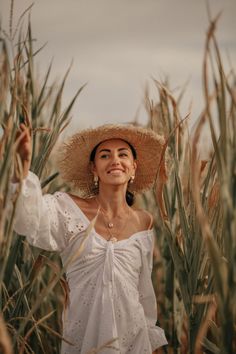 a woman wearing a straw hat standing in a corn field with her arms out to the side