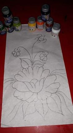 a white paper with flowers drawn on it next to some paint cans and paints in front of it