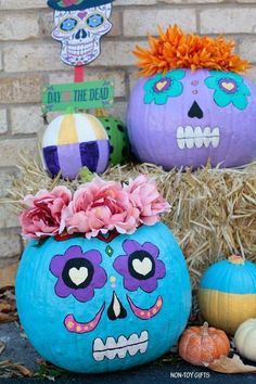 three pumpkins decorated with sugar skulls and flowers in front of a brick wall on hay bales