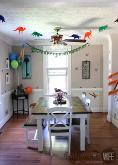 a dining room table with dinosaur decorations on the ceiling and balloons in the air above it