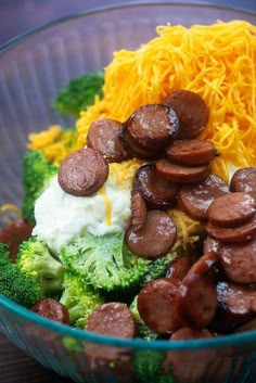 a glass bowl filled with broccoli, cheese and sausage on top of it