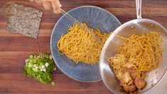 two plates with noodles and vegetables on a wooden table