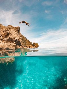 a bird flying over the ocean near a rocky island with clear water and blue skies