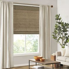 a living room with a couch, coffee table and window covered in white drapes