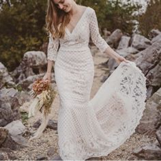 a woman in a white dress is walking on some rocks and holding a lace shawl