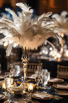 a tall vase filled with white feathers sitting on top of a table covered in gold plates