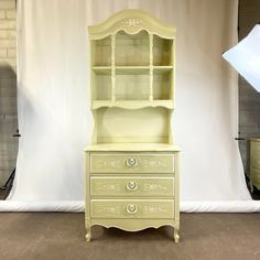 a white dresser with drawers in front of a backdrop