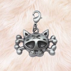 a silver cat charm with skulls and bones on it's face, sitting on a furry surface