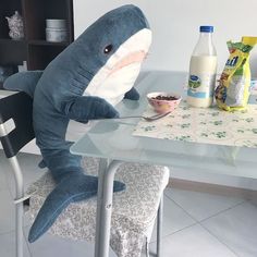 a stuffed shark sitting on top of a glass table next to a bowl of cereal