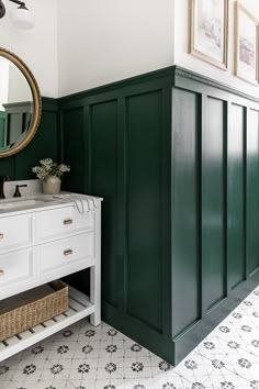 a bathroom with dark green walls and white drawers, an oval mirror on the wall