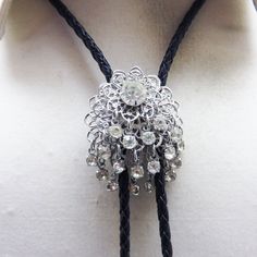 This vintage shiny  silvertone filigree metal bolo tie slide is roughly round in shape.  But the attached white rhinestones, give it movement and sparkle.  This bolo is big and bold and dazzling in its brilliance. The bolo slide measures 1 3/4 inches tall and 1 1/2 inches wide and is placed on a 36 inch  black leatherette string tie with silverplated metal end caps . It is in excellent condition .  This was made with vintage pieces in our Montana Rock Shop.   We will send this in a lovely gift b Silver Lariat Bolo Ties For Formal Occasions, Silver Lariat Bolo Tie For Formal Occasions, Elegant Silver Bolo Tie As Gift, Elegant Silver Bolo Ties As A Gift, Elegant Concho Bolo Tie, Vintage Silver Bolo Ties As Gift, Western Silver Lariat Bolo Ties, Vintage Bolo Ties With Adjustable Length For Rodeo, Vintage Silver Engraved Bolo Ties