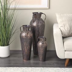 three vases sitting next to each other in front of a white couch and potted plant