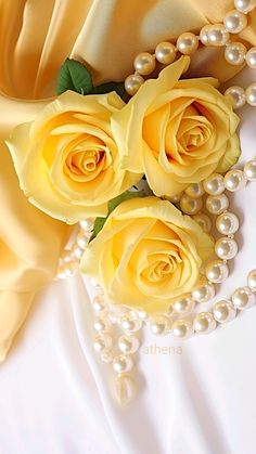 three yellow roses and pearls on a white satin background with a beaded necklace in the foreground