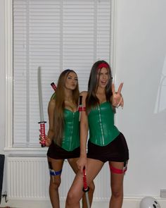 two women dressed in cosplay clothes holding swords and making the peace sign with their hands