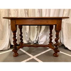 an old wooden table with turned legs on the floor in front of curtained windows