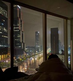 a person sitting in front of a window looking out at the city lights and skyscrapers