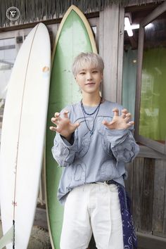 a young man standing next to two surfboards in front of a building and holding his hands out