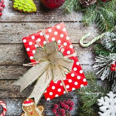 presents wrapped in red and white paper with christmas decorations around them on a wooden table