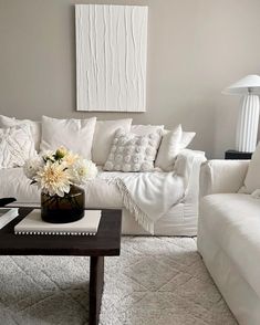 a living room filled with white furniture and flowers in a vase on top of a coffee table