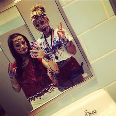 a man and woman in zombie makeup standing in front of a bathroom mirror holding up their hands