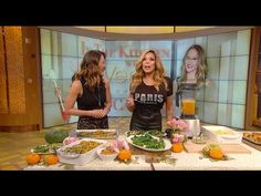 two women standing in front of a table full of food and drinks on the set of news