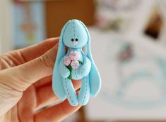 a hand holding a tiny blue bunny with flowers in it's lap and the top part of its body