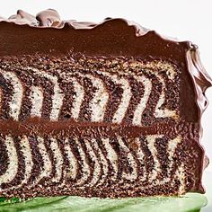 a piece of chocolate cake with white and brown frosting on it sitting on top of a green leaf