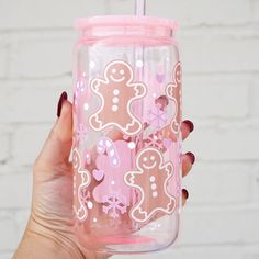 a hand holding a pink and white cup with gingerbreads on the side, in front of a brick wall