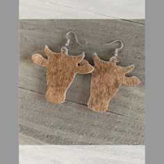 two deer head shaped wooden earrings hanging from silver earwires on a wood surface