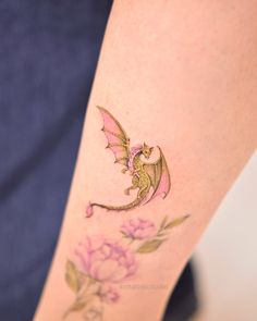 a woman's leg with a dragon tattoo on it and flowers in the background