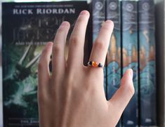 a person's hand with a ring on it in front of bookshelves